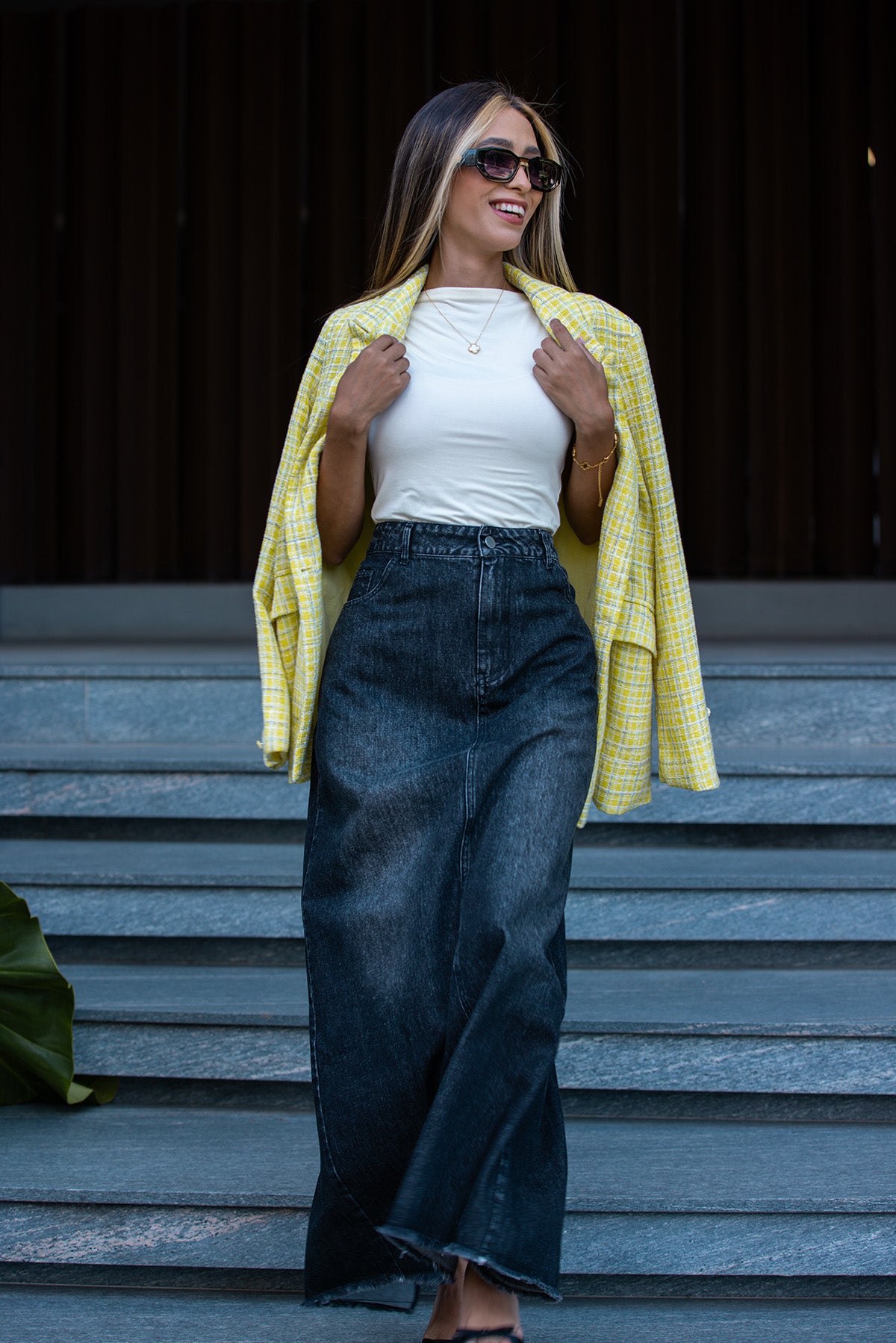 Woman wearing a yellow jacket, white top, and dark jeans standing on steps. Fine Modesty