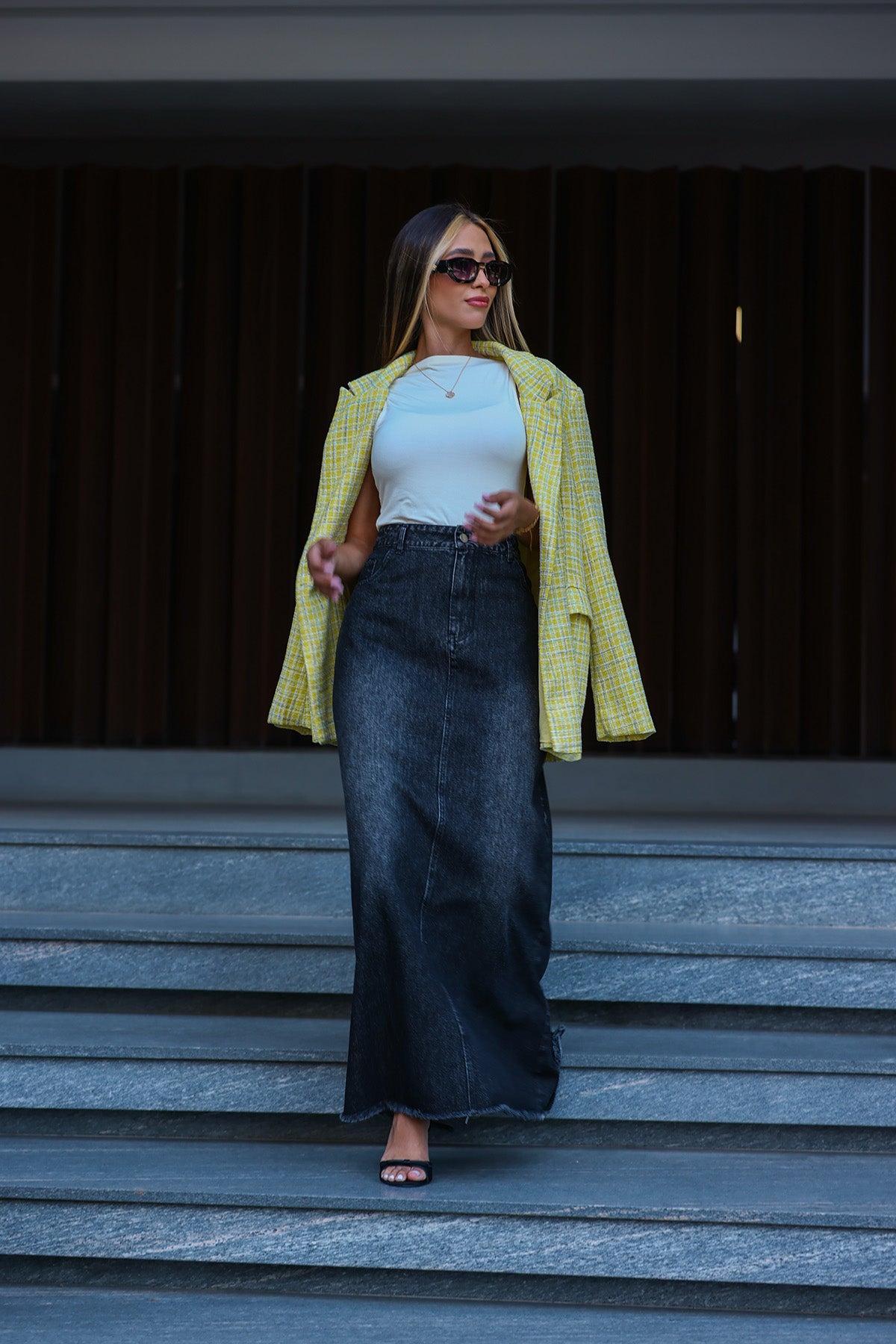 Woman in a yellow jacket, white top, and black pants standing on steps. Fine Modesty