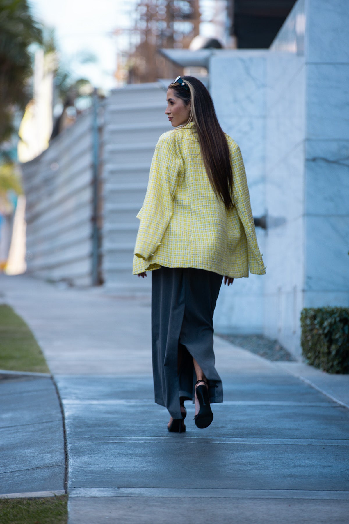 Woman in a yellow jacket and gray skirt walking on a sidewalk. Fine Modesty